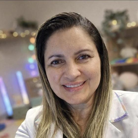 Retrato de Eliana Arantes, terapeuta ocupacional, sorrindo, de jaleco branco